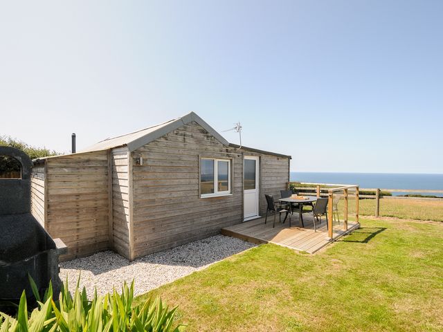 A wooden cabin with a small deck and outdoor table and chairs overlooking the sea at Lundy View Chalet in Widemouth Bay