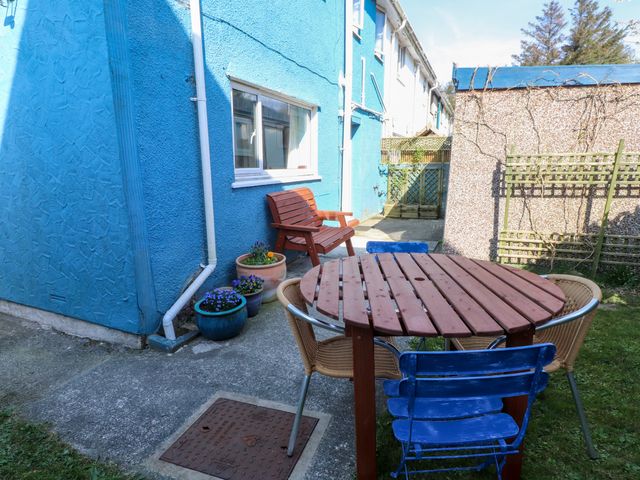 A small outdoor patio with a round wooden table surrounded by chairs and a small wooden bench against a blue painted wall at 11 Penygroes in Llanddeusant