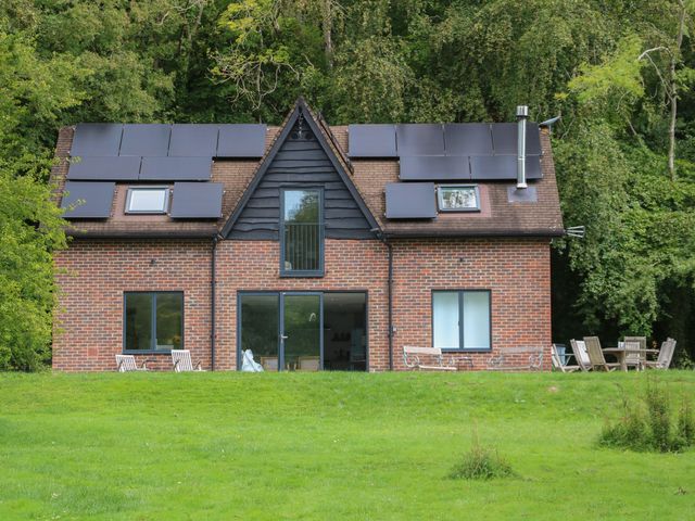 A brick house with solar panels on the roof and outdoor furniture on a lawn at Meon Boscage in Meonstoke