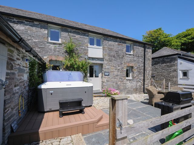 A stone cottage with a hot tub on a wooden platform and outdoor seating with a barbecue at Courtyard Cottage within the Helland Barton Farm collection in Delabole