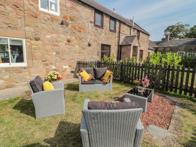 An outdoor seating area with gray wicker furniture and cushions in a garden beside a stone building at O'Neil Cottage in Beadnell