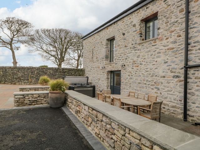 An outdoor patio area with a wooden table and chairs stone walls and large planters at Old Stable in Roose