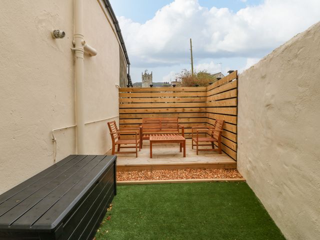An outdoor seating area with wooden chairs and a table on a wooden deck next to a grassy area at Glanffrwd - Nefyn in Nefyn