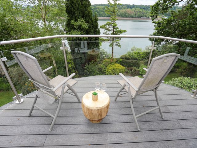 Two chairs and a small table with glasses on a balcony overlooking a river and trees at Ynys Castell in Menai Bridge