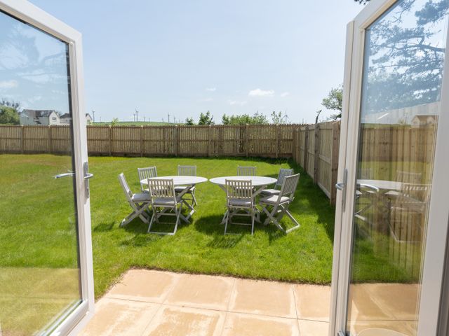 An outdoor patio area with two round tables and several chairs on green grass behind glass doors at The Bright House in St Eval near St Columb Major