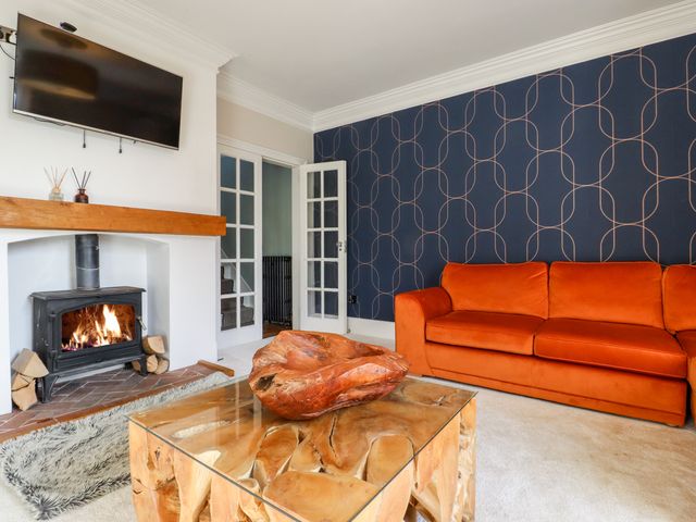 A living room with a wood burning stove and orange sofa at Crud Yr Awel in Bridge Kent