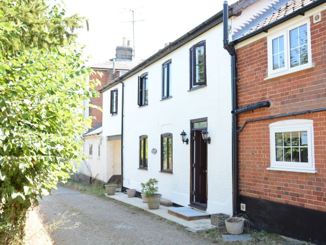 A white two-story house with black window frames and door next to a red brick building under trees at Pine Cottage in Woodbridge