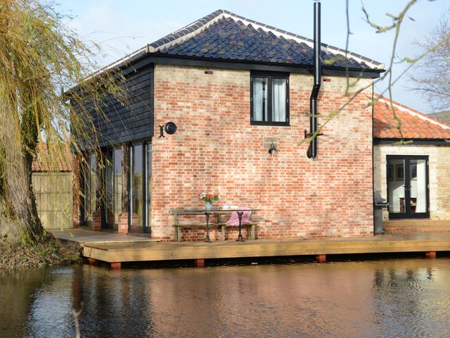 A brick house with black window frames and a tiled roof next to a wooden deck and water at Fishpond House Sotherton in Halesworth