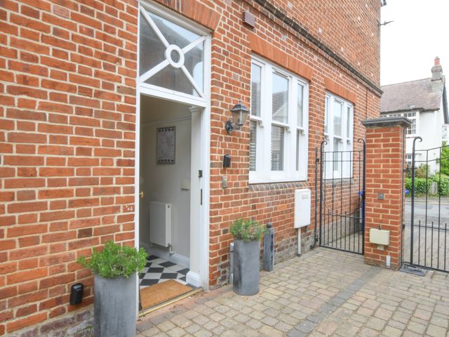 An open doorway with two tall planters outside a red brick building with windows and a black metal gate at 1 Eversley Court Southwold