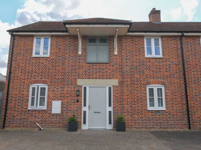 A brick building with white framed windows and a central gray door with two small plants at the entrance at 1 Coconut Cottage Long Melford