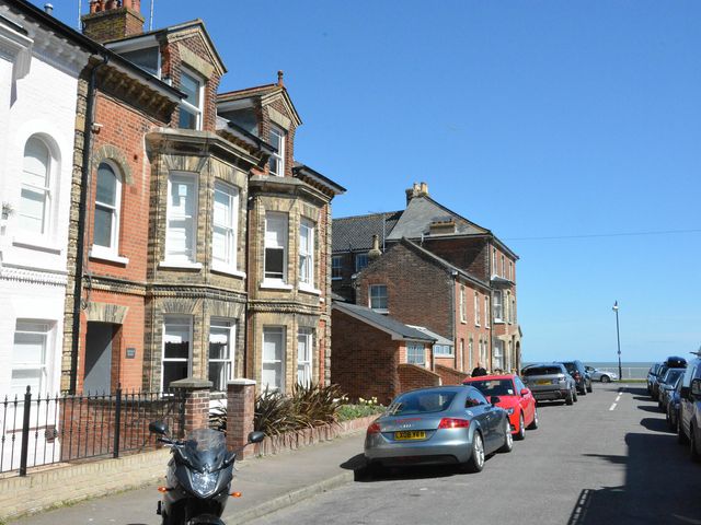 A street with parked cars and brick houses under a clear blue sky at Osprey in Southwold