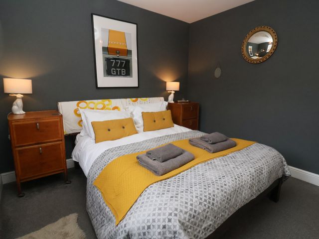 A bedroom with a double bed yellow cushions bedside tables lamps and a framed picture on the wall at Kestrel in Southwold