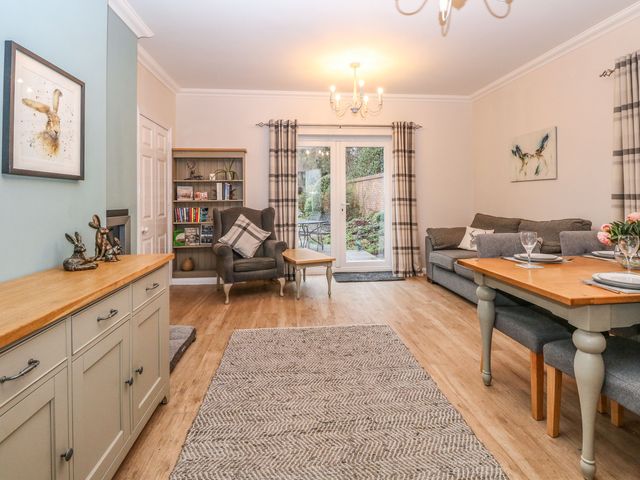 A living room with armchair bookshelf sofa and dining table near glass doors at Brundall House in Brundall