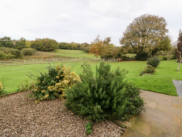 A garden with stone path, shrubs, and a grassy field with trees and a wooden fence at Cae Du in Dwyran near Niwbwrch Newborough