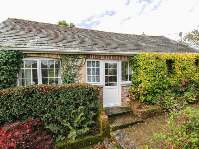 Exterior view of a stone cottage with white framed windows and door surrounded by shrubs and climbing plants at The Wagon House Lezant near Launceston