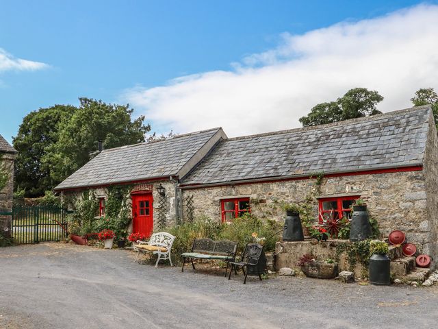 A cottage with a red door, benches, and flower pots at The Dairy in Ardfinnan, County Tipperary