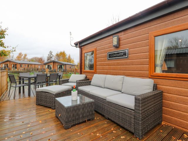 An outdoor seating area with wicker furniture and a dining table on a wooden deck at Clearwater in Warton near Carnforth