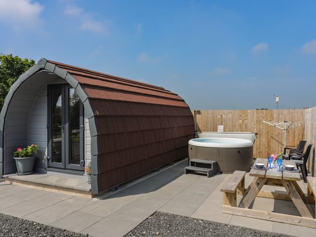 An outdoor area with a small pod structure a hot tub a wooden picnic table and chairs at Parys Pod in Amlwch