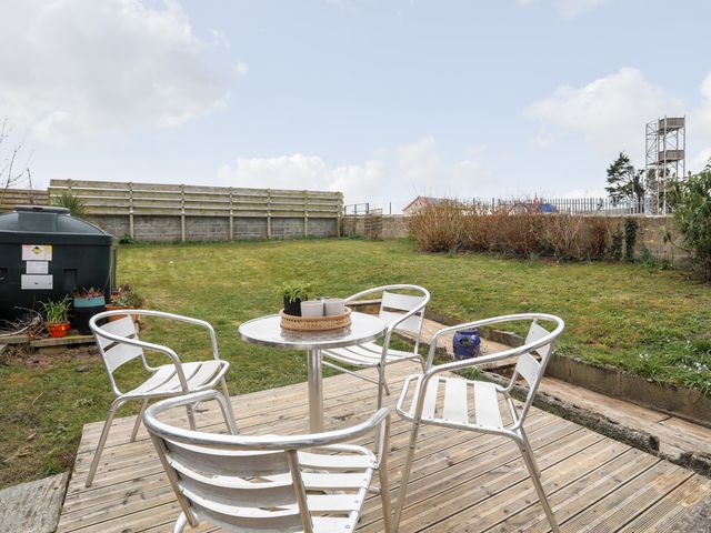 An outdoor patio area with metal chairs and a table on wooden decking in a garden at 2 Trem-Y-Mor in Rhosneigr