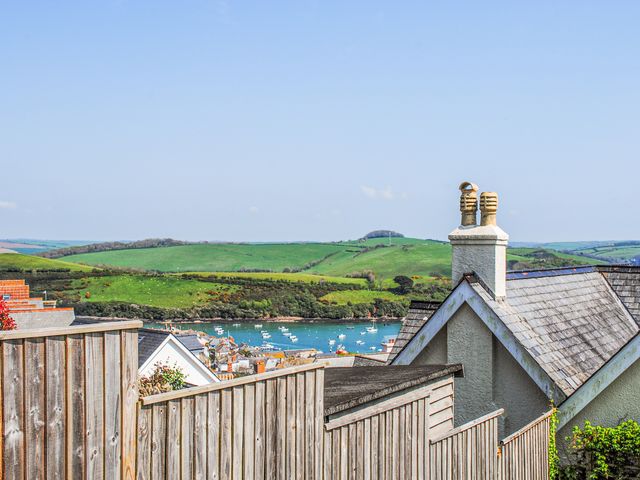 A view of rooftops wooden fences a body of water with boats and green hills in the background at Waders in Salcombe