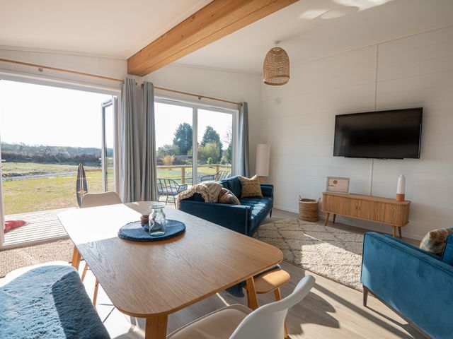 A living room with blue sofas a wooden dining table and a wall-mounted TV at Galwad y Mor in Niwbwrch newborough