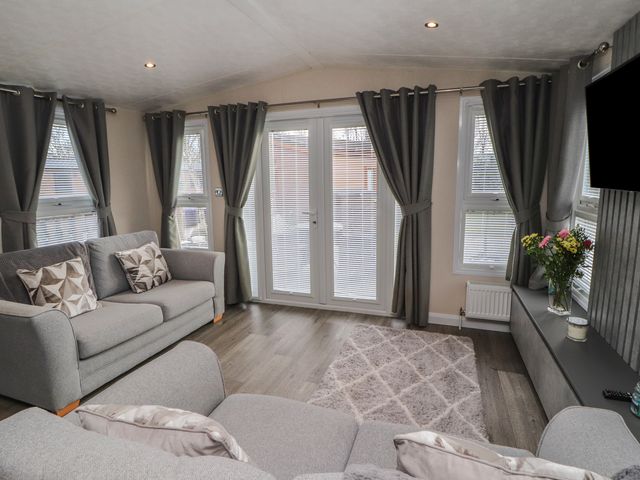 A living room with sofas pillows curtains a rug flowers on a table and a television at 24 Sherwood in Carnforth