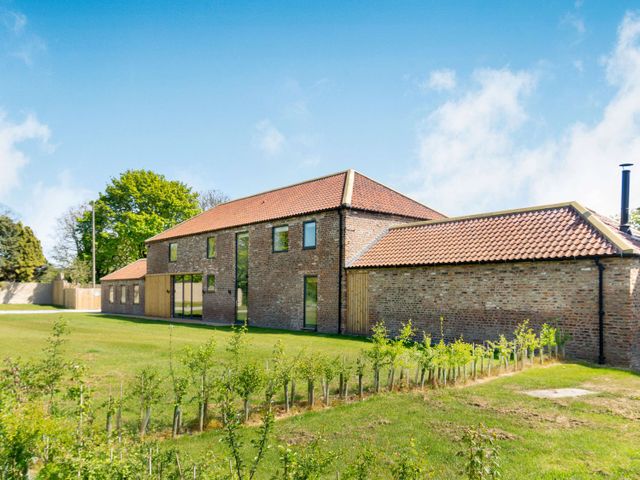 A brick house with a tiled roof and multiple glass windows surrounded by grass and small plants at Fox's Den in Burton Pidsea