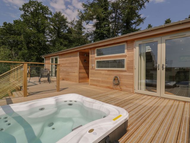 A wooden deck with a hot tub a table and chairs outside a building with glass doors and trees in the background at 2 Faraway Fields in Dobwalls