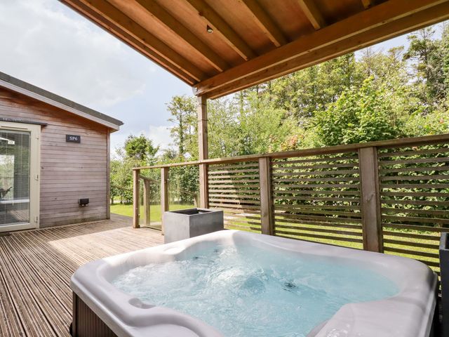 An outdoor wooden deck with a hot tub under a covered roof and wooden railing surrounded by greenery at 6 Southern Place in Dobwalls