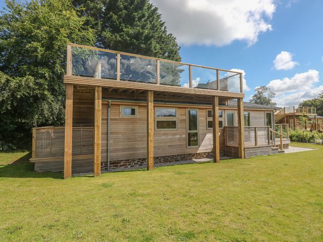 An exterior view of a wooden house with large grass lawn and balcony with glass railing at 2 Southern Place in Dobwalls