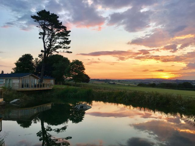 A pond reflecting trees and a cabin with a sunset over fields in the background at 12 Faraway Fields in Dobwalls