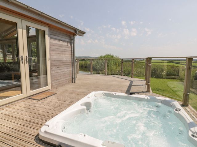 An outdoor hot tub on a wooden deck next to a building with glass doors overlooking green fields at 15 Faraway Fields in Dobwalls