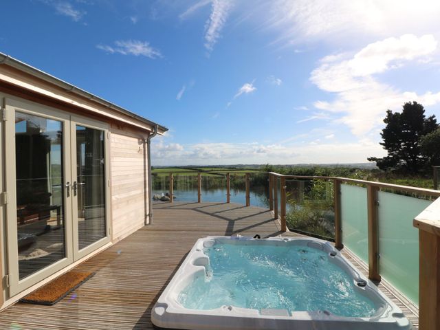 An outdoor deck with a hot tub and glass railing overlooking a body of water at 14 Faraway Fields in Dobwalls
