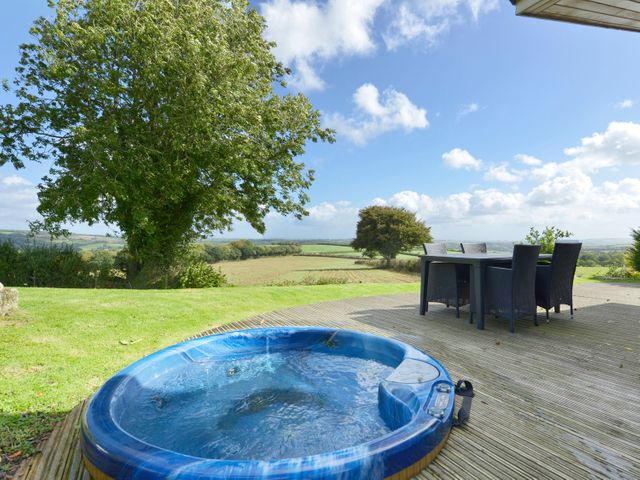 A backyard with a hot tub and outdoor dining furniture overlooking fields and trees at 10 Horizon View in Dobwalls