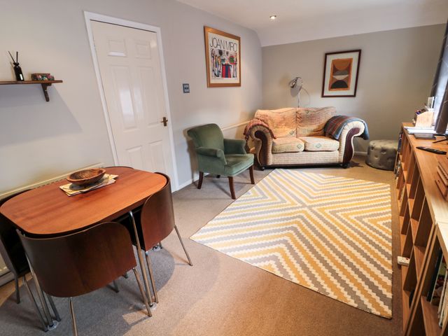 A living room with a wooden dining table and chairs a green armchair a small sofa a patterned rug and framed artwork on the walls at 60B Castlegate in Berwick-Upon-Tweed