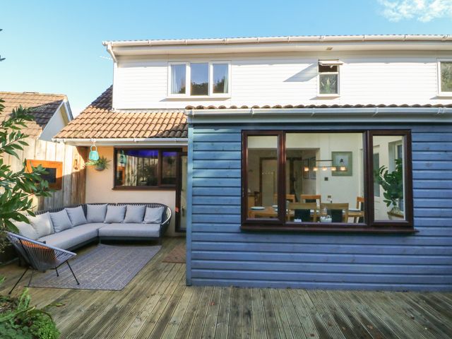 An outdoor patio with a sectional sofa and chair next to a wooden house with large windows at Hillsview in Combe Martin