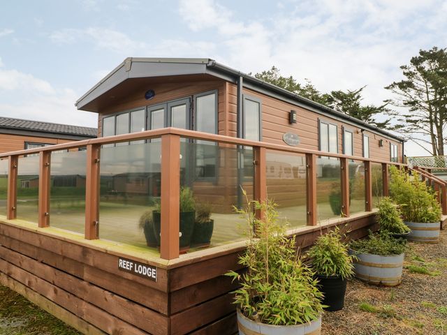 An exterior view of a wooden lodge with glass railing and potted plants outside at Reef Retreat in Broad Haven