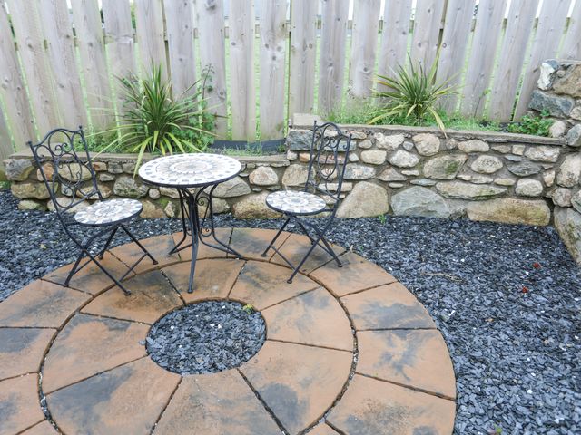 A small outdoor patio with a round mosaic table and two matching chairs surrounded by a stone wall and gravel at Tyn Lon - Y Ffor in Y Ffor near Pwllheli