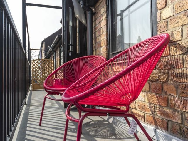 A narrow outdoor balcony with two red chairs and a black railing at Old Bakery No2 in Seahouses