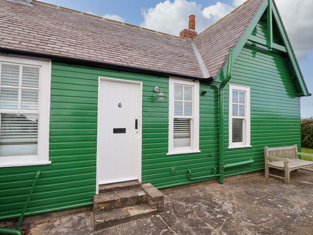 The exterior of a green wooden house with a white door numbered 6 two windows and a wooden bench outside at Armstrong Cottages No6 in Bamburgh