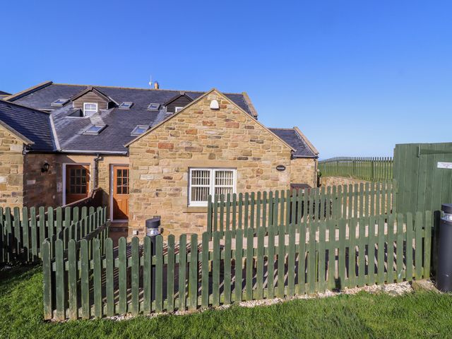 An outdoor area with a stone house and a green fence at Goosander in Bamburgh