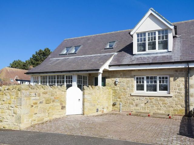 A stone cottage with a white gate and multiple windows under a blue sky at Stone Cottage in Bamburgh