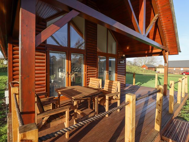 A wooden porch with a table and chairs outside a log cabin at Lodge 7 in South Hykeham