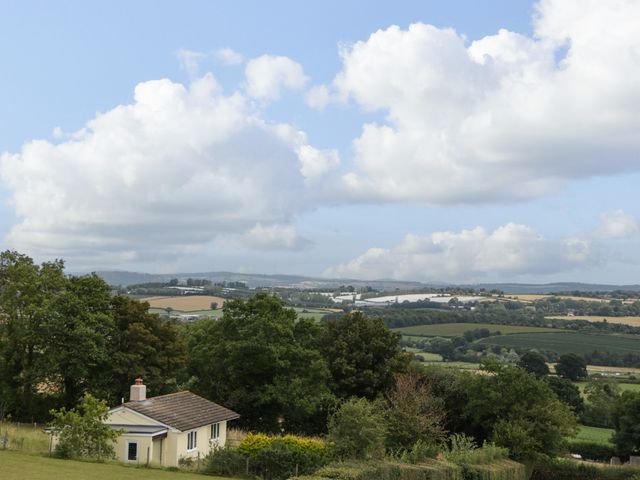 A rural landscape with a small house surrounded by trees and fields under a partly cloudy sky at Palace Bungalow in St Weonards