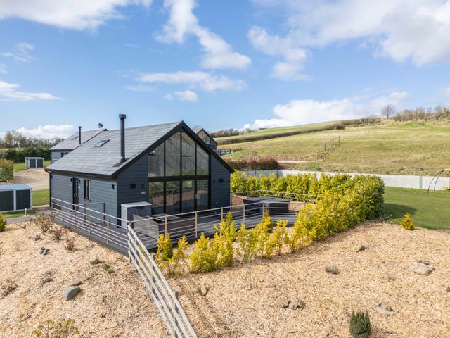 A modern house with large glass windows and a fenced garden surrounded by grassy hills at Stags Mount in Thornton Dale