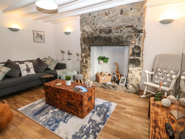 A living room with a stone fireplace a dark sofa wooden coffee table and a rocking chair at Cudfan Fach in Llithfaen
