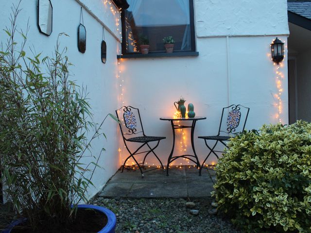 An outdoor seating area with two metal chairs and a small round table with lights stringed on the wall and table at Capel Zion Burwen near Amlwch