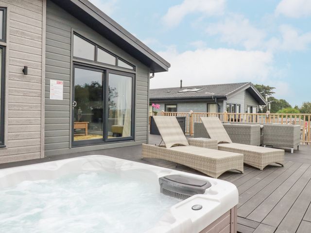 An outdoor deck with two lounge chairs a hot tub and a seating area outside a modern cabin at Mordros Lodge in St Day
