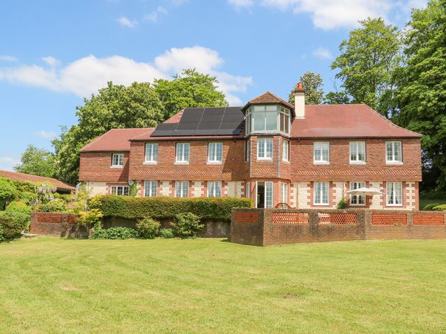 An exterior view of a two story house with solar panels on the roof surrounded by grass and trees at Coombe Place House in Meonstoke