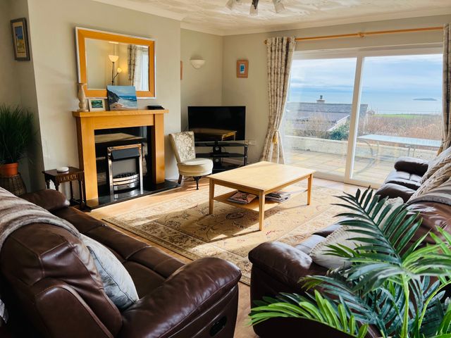 A living room with brown leather sofas a wooden coffee table and a fireplace with a mirror above at Garna Mynytho near Llanbedrog